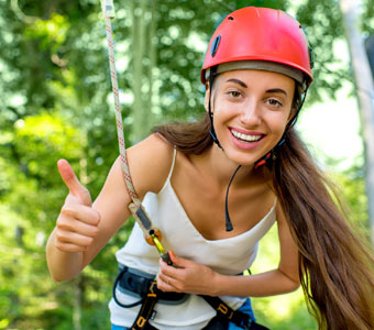 girl with a helmet on smiling and giving a thumbs up during a canopy tour